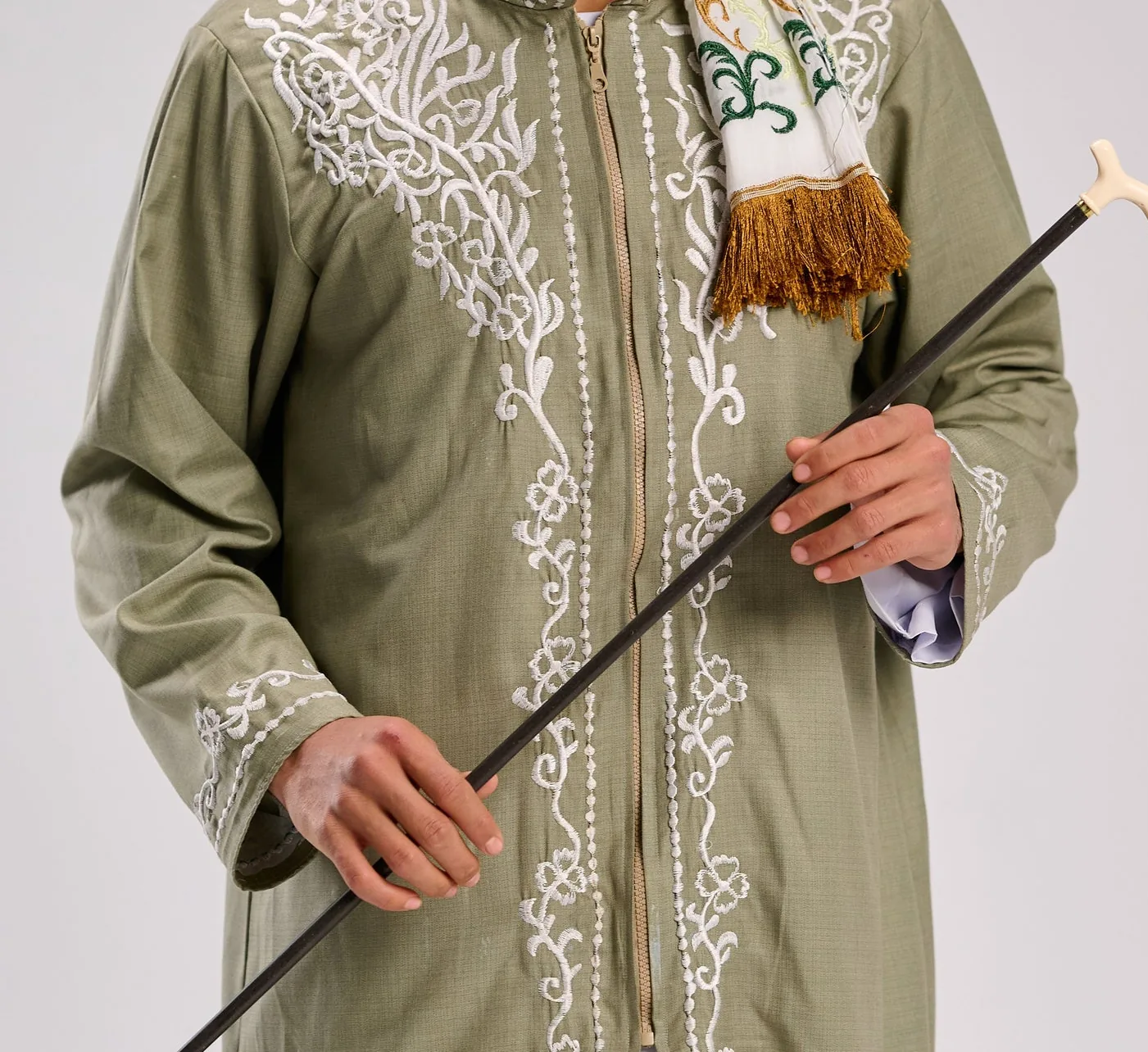 White floral embroidery detail across the chest of a sage-green linen thobe.