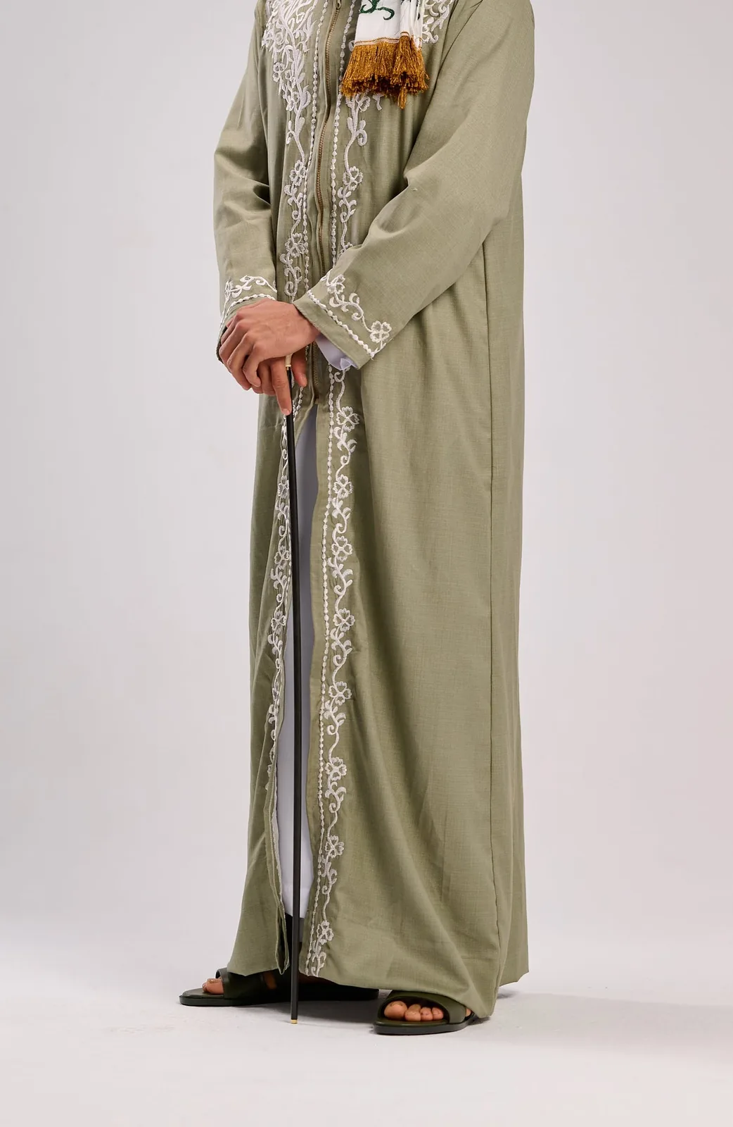 Full-length drape of an embroidered sage-green thobe on a seamless grey background.